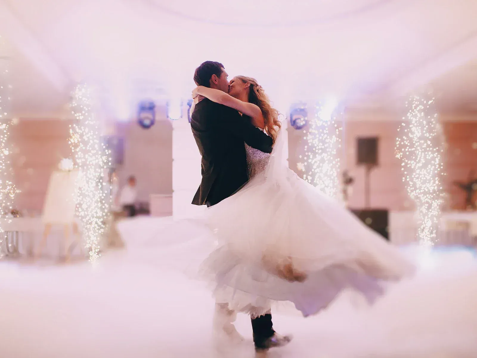 A bride and groom dancing in a wedding reception hall with sparkler fountains in the background.